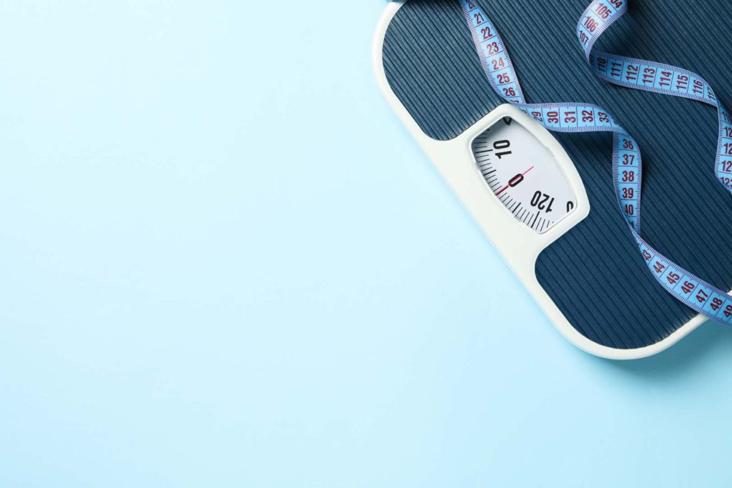 Scales and measuring tape on blue background. Weight loss concept
