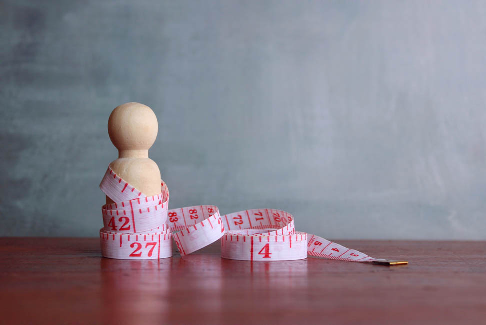 Diet and weight management concept. Wooden doll and measuring tape. Copy space for text.