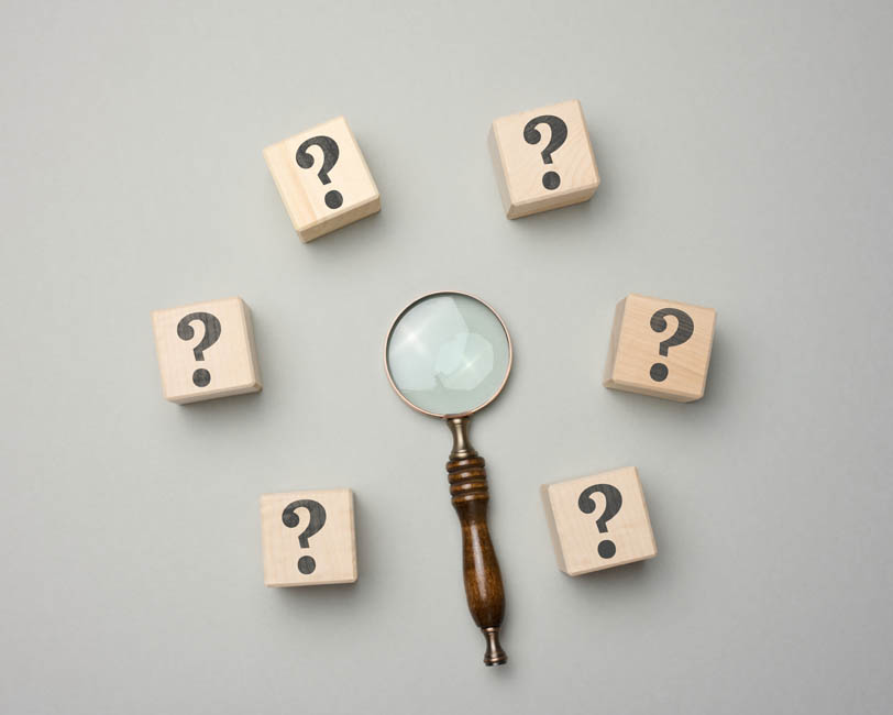 Wooden magnifier and cubes with question marks on gray background. Сoncept of finding an answer to questions, truth and uncertainty. Answers on questions