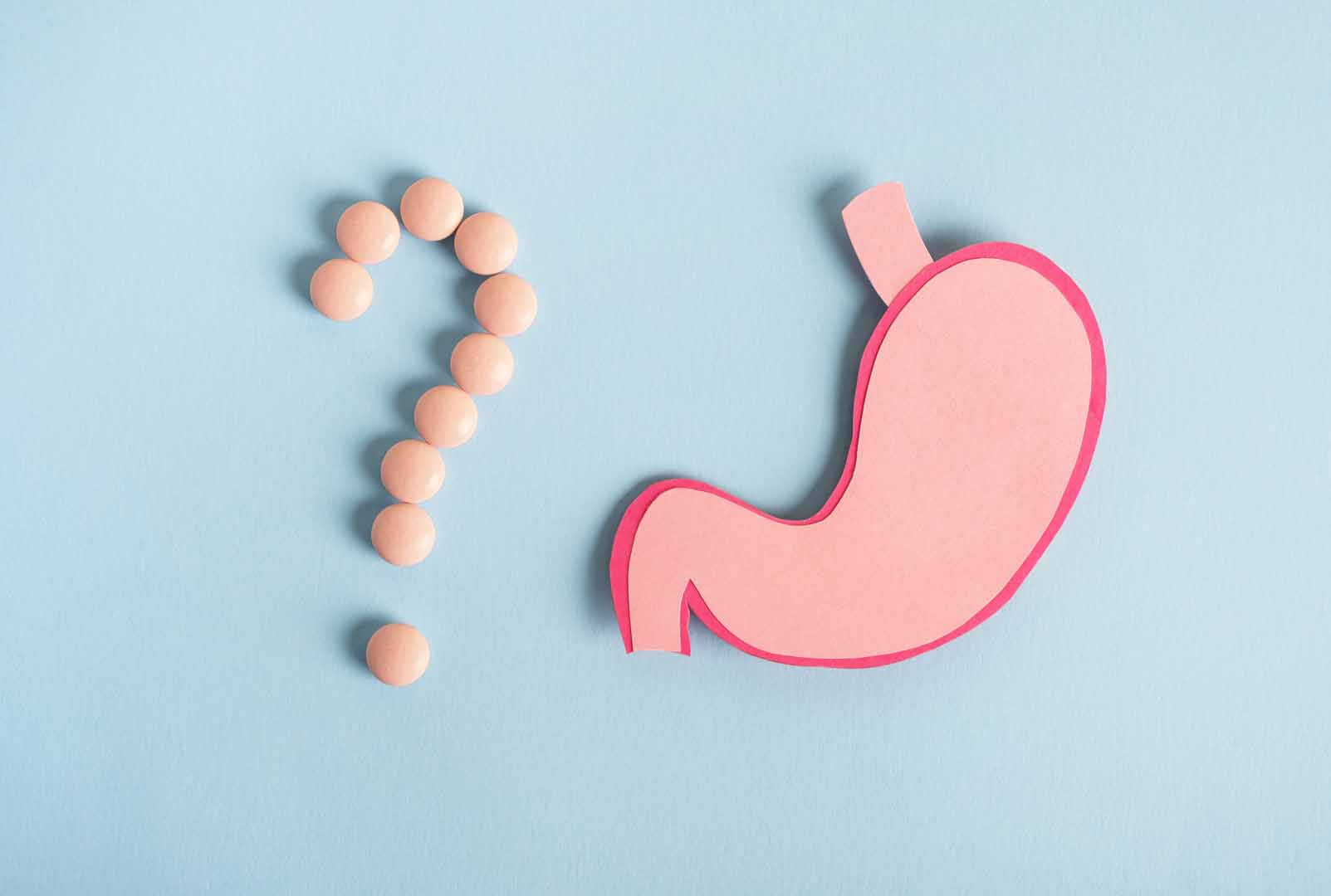 Stomach decorative model with pills in shape question mark on light blue background